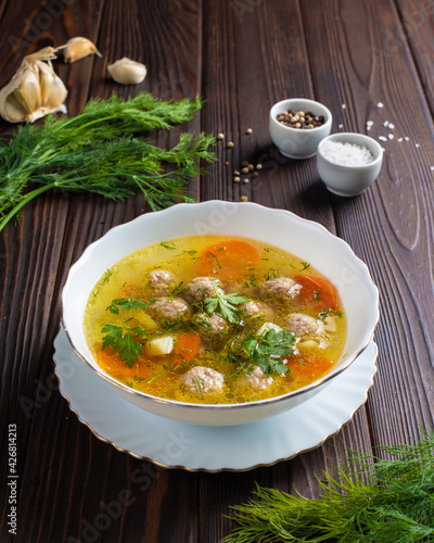 Soup with meatballs in a white plate with sauce and herbs on a wooden table. Photo for the menu of a restaurant, cafe, canteen. 
