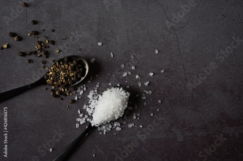 Spoon full of sea salt and black pepper on dark grey stone background. 