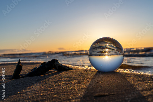 a glowing sunset can be seen through a glass ball. near the crystal ball in the sand is a tree branch