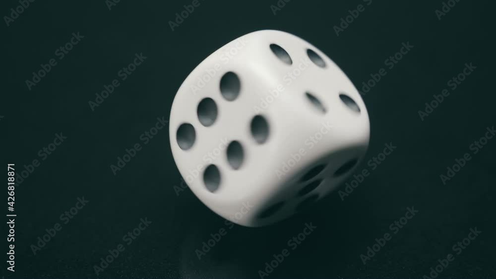 On a black background, a white dice cube (a symbol of gambling in a casino) rotates around its axis for a long time and leaves the frame. Macro. Closeup. Slow mo, slo mo, slow motion, high speed camer On a black background, a white dice cube (a symbol of gambling in a casino) rotates around its axis for a long time and leaves the frame. Macro. Closeup. Slow mo, slo mo, slow motion, high speed camer