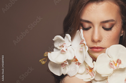 Attractive model woman with healthy clear skin and spring orchid flowers. Facial treatment and skin care concept