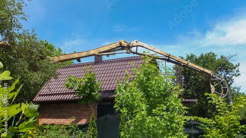 Concrete pump pipe delivers concrete through roof of two-story house. Pouring foundation with concrete using concrete pump. Construction of building in confined space. Close-up.