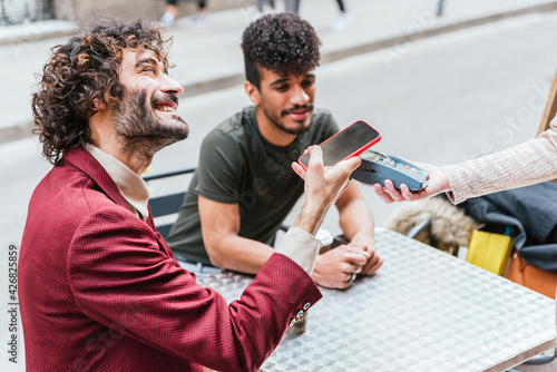 Photography detail of a younc caucasian man using his phone to make a payment in a cafeteria