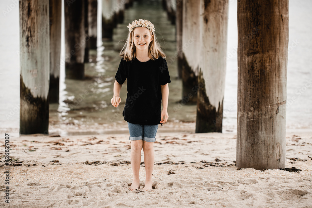 Caucasian girl standing underneath a pier at the beach wearing a flower head band Caucasian girl standing underneath a pier at the beach wearing a flower head band
