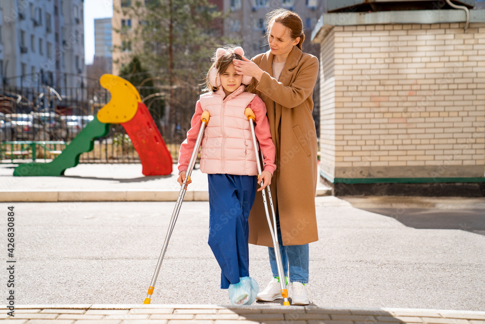 mom helps daughter learn to walk on crutches. plaster on your feet