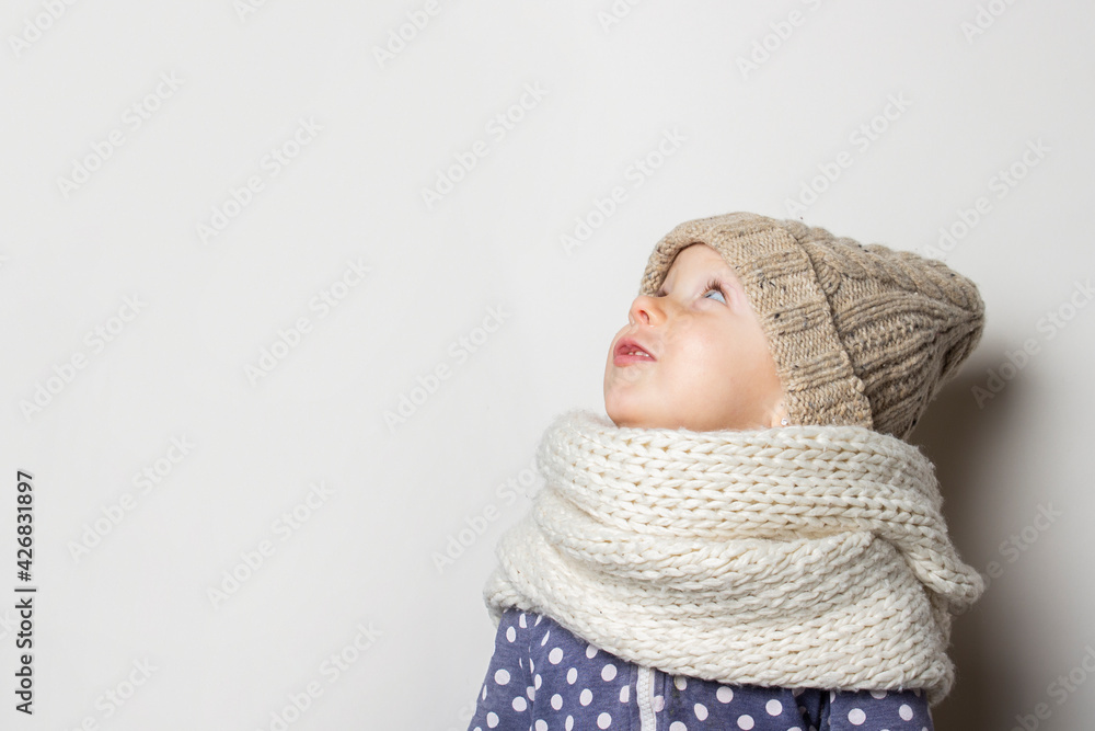 beautiful little baby in a hat looks away on a light background. Concept of children's emotions, winter, shopping