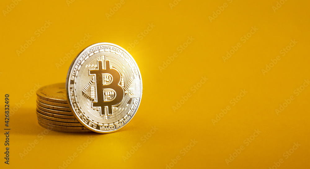 A bitcoin resting on a pile of bitcoins on a yellow background and copy space. Golden BTC coin, Stock Market of cryptocurrencies and decentralized finances concept