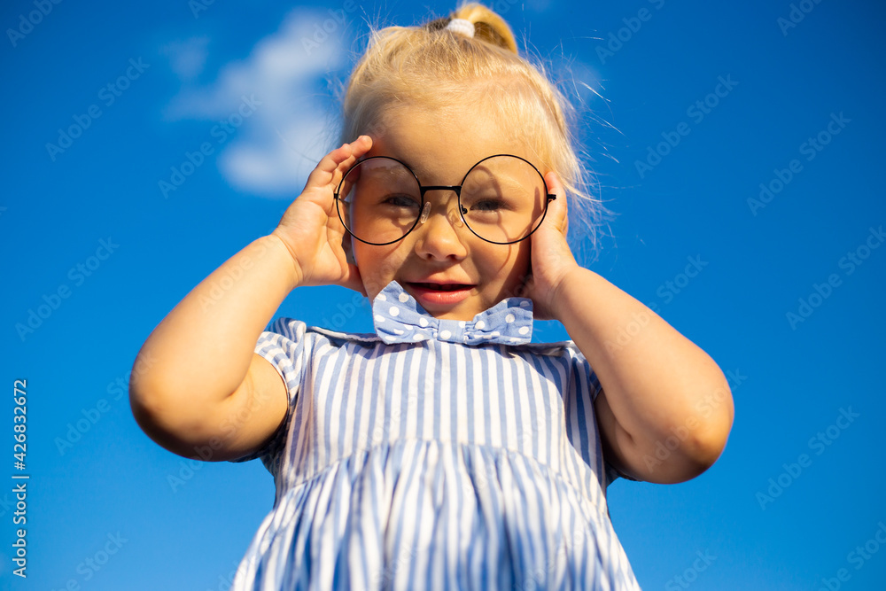 Little girl in dress and glasses on a background of blue sky