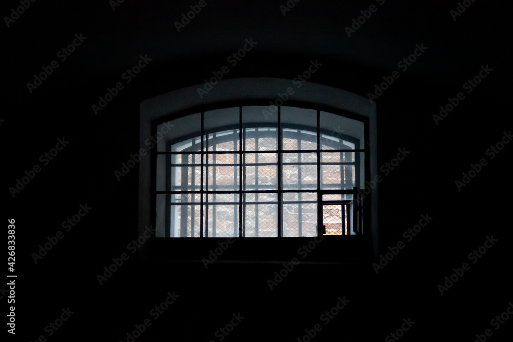 A window in a prison cell, covered with bars. The interior of an old dark solitary prison cell. A window in a prison cell, covered with bars. The interior of an old dark solitary prison cell.