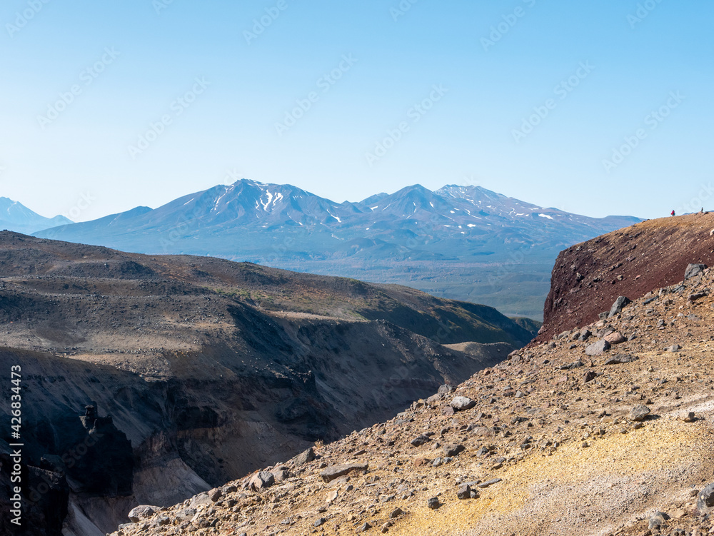 View of the Opasny canyon near the Mutnovsky volcano. Tourists stand near the edge of the canyon and admire incredible views of the volcanoes. Kamchatka Peninsula, Russia.