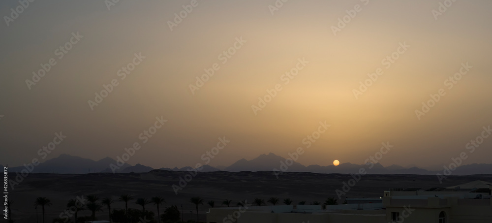 The sun sets behind the mountains against the backdrop of a sandy desert. Egypt.