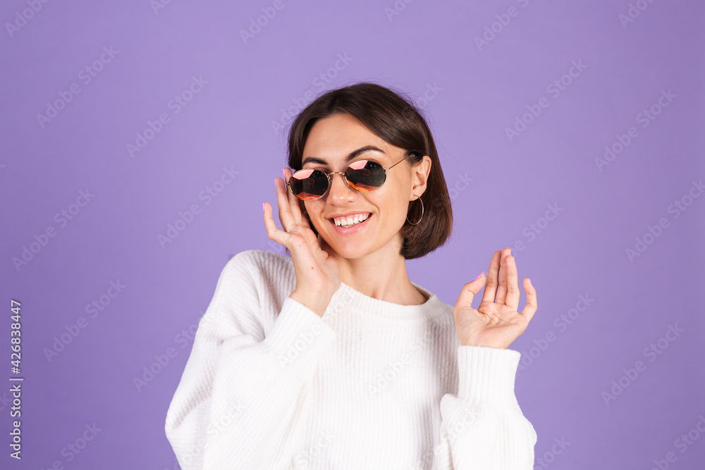 Young brunette in white casual sweater isolated on purple background wearing sunglasses happy smile positive moving Young brunette in white casual sweater isolated on purple background wearing sunglasses happy smile positive moving