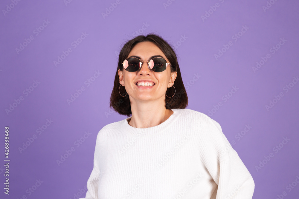 Young brunette in white casual sweater isolated on purple background wearing sunglasses happy smile positive moving Young brunette in white casual sweater isolated on purple background wearing sunglasses happy smile positive moving