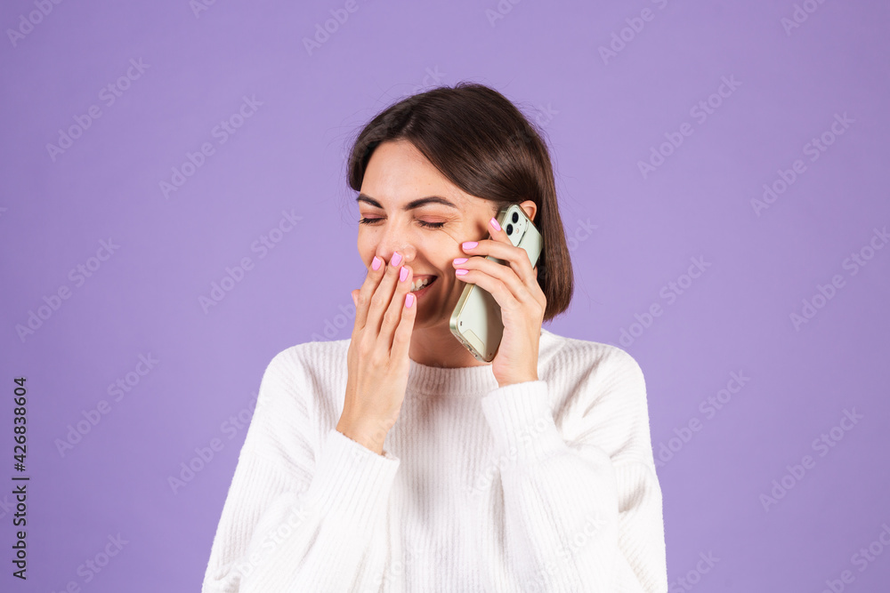Young brunette in white casual sweater isolated on purple background having conversation with happy mood, talking positive on mobile phone, smiling Young brunette in white casual sweater isolated on purple background having conversation with happy mood, talking positive on mobile phone, smiling