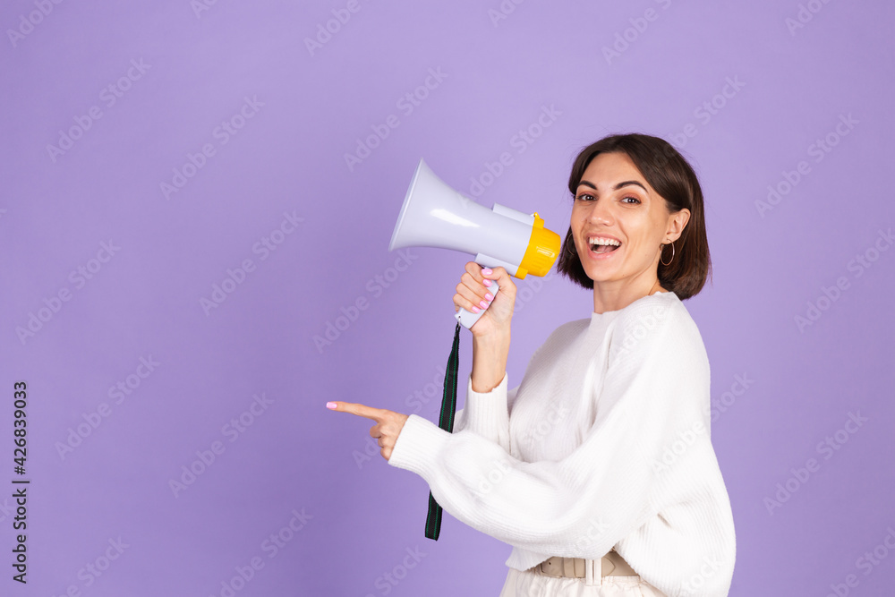 Young brunette in white casual sweater isolated on purple background happy screaming in megaphone copy space point left Young brunette in white casual sweater isolated on purple background happy screaming in megaphone copy space point left