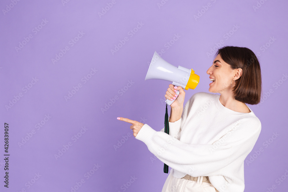 Young brunette in white casual sweater isolated on purple background happy screaming in megaphone copy space point left Young brunette in white casual sweater isolated on purple background happy screaming in megaphone copy space point left