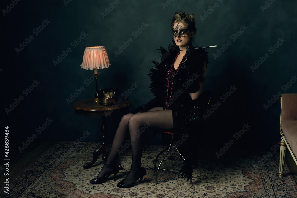 Mysterious young woman with a black boa and mask in retro boudoi