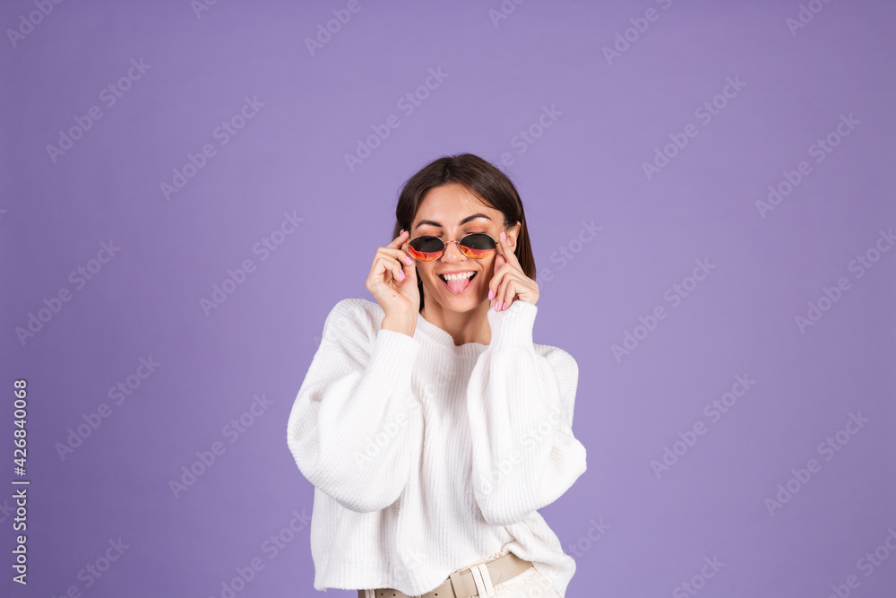 Young brunette in white casual sweater isolated on purple background in sunglasses happy funny playful shows tongue Young brunette in white casual sweater isolated on purple background in sunglasses happy funny playful shows tongue