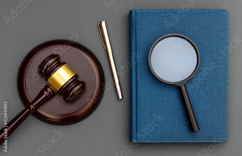Magnifying glass with judge gavel and notepad on black background. Top view.