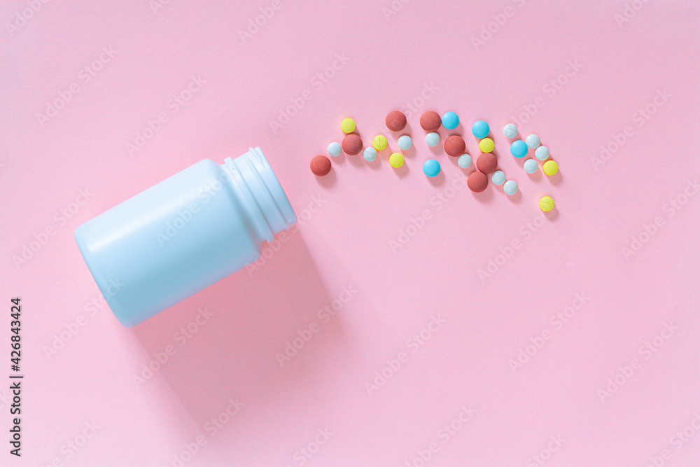 Multicolored tablets, pills, capsules in plastic bottle on pink background, copy space. Medicine, vitamin and nutritional supplements concept. Multicolored tablets, pills, capsules in plastic bottle on pink background, copy space. Medicine, vitamin and nutritional supplements concept.