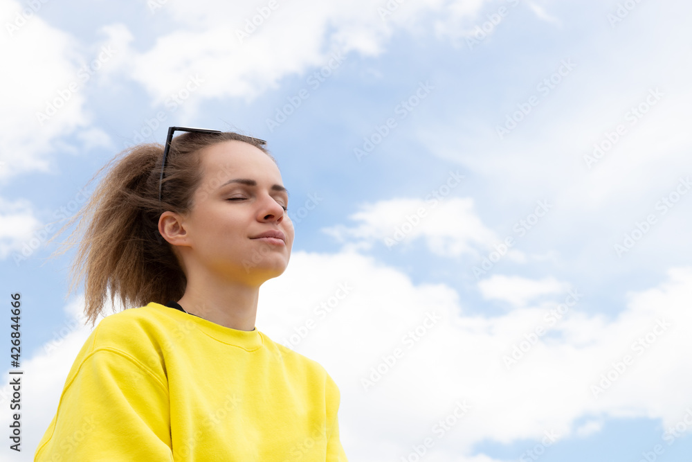 The candid young woman stands under high blue sky with closed eyes enjoying life and moment. Female Portrait on sky background with copy space. The candid young woman stands under high blue sky with closed eyes enjoying life and moment. Female Portrait on sky background with copy space.