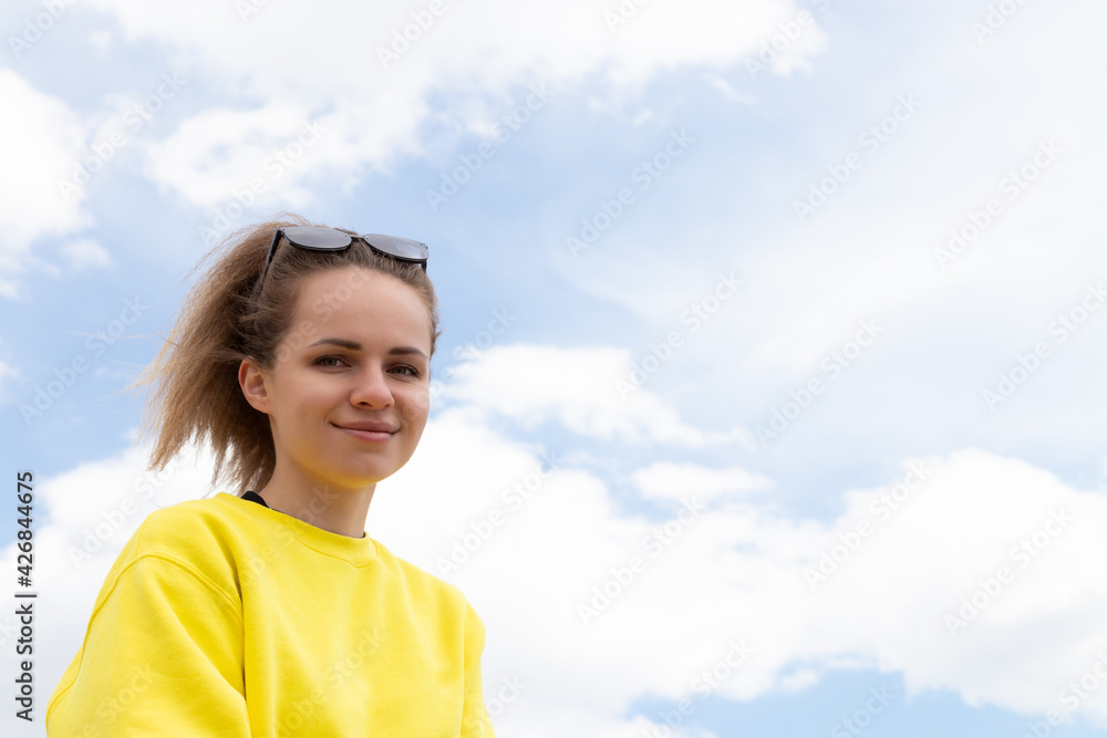Beautiful brunette young woman is happy and smiling stands under blue sky. Portrait of pretty girl wearing yellow sweatshirt. Beautiful brunette young woman is happy and smiling stands under blue sky. Portrait of pretty girl wearing yellow sweatshirt.