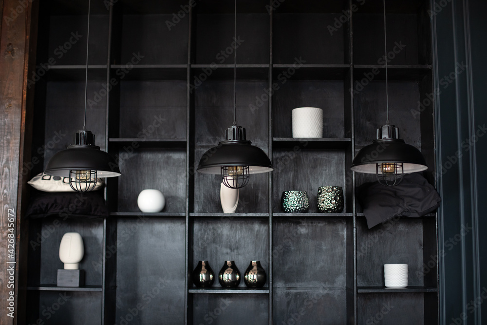 Metal chandeliers in retro style on background wooden shelves with decor. Dark room with Three modern lamps over table. Three modern black ceiling lamps hang in room, close-up. Loft room interior.	