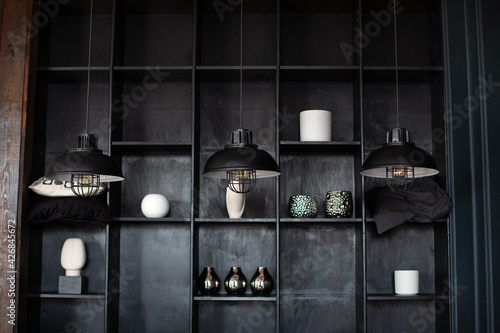 Metal chandeliers in retro style on background wooden shelves with decor. Dark room with Three modern lamps over table. Three modern black ceiling lamps hang in room, close-up. Loft room interior. 