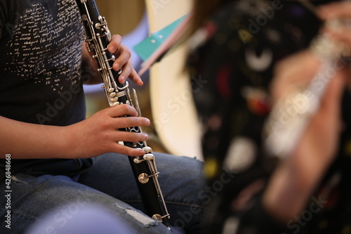 A young hand of a student musician presses the valves of a black clarinet musical instrument with his fingers at a school orchestra class.Background image.Close-up.Music Training