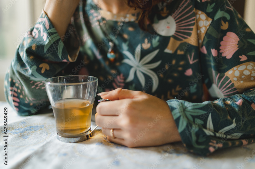 Unrecognizable woman just waked up wearing pajamas sitting at table drinking and holding a cup of hot tea. Unrecognizable woman just waked up wearing pajamas sitting at table drinking and holding a cup of hot tea.