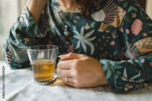 Unrecognizable woman just waked up wearing pajamas sitting at table drinking and holding a cup of hot tea.