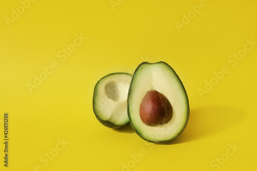 two halves of cut avocado fruit on yellow background