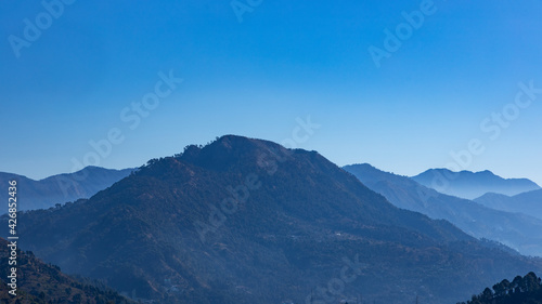 A panoramic view of silhouette of layers of mountains with fog in the valley and clear blue sky