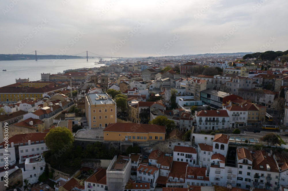 Aerial drone view over Alfama District, Lisbon, Portugal. Lockdown cityscape. Commerce plaza in Downtown. 25 April bridge over Tagus River.