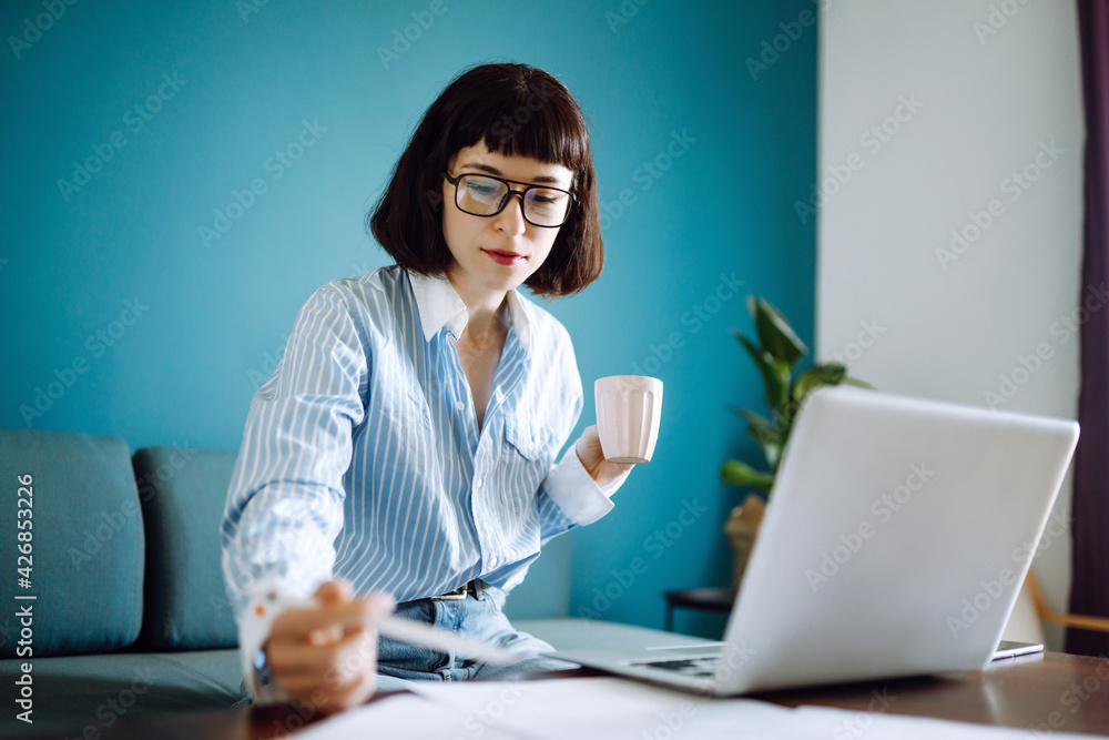 Beautiful woman working on laptop computer while sitting at the living room, drinking coffee. Technology, freelance, shopping online, remote work, E learning concept. Beautiful woman working on laptop computer while sitting at the living room, drinking coffee. Technology, freelance, shopping online, remote work, E learning concept.