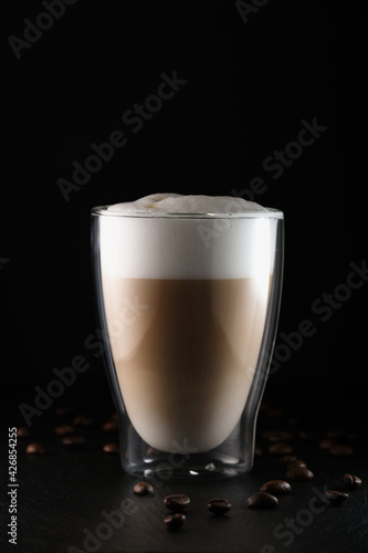 Italian latte macchiato on a black background. Cappuccino, glass cup with double walls on a black background. Cappuccino in a transparent cup. Latte macchiato, coffee beans on black.