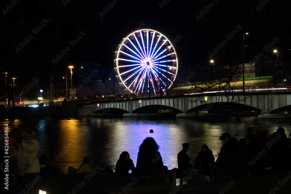 Beautiful illuminated ferris wheel at city of Zurich at Friday night with river Limmat. Photo taken April 9th, 2021, Zurich, Switzerland.