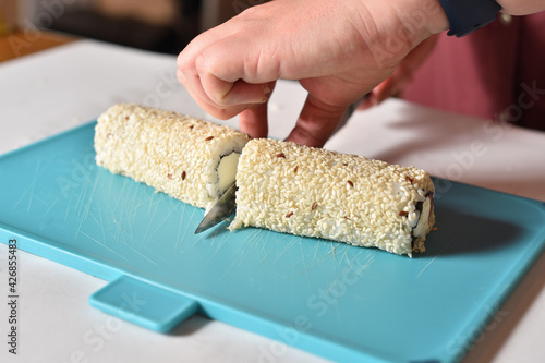 Chef cuts fresh cooked sushi roll with curd cheese and sesame
