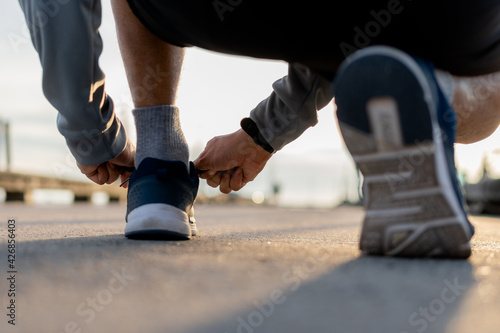 Man tying running shoes on road outdoor. Male preparing for a run exercise workout in the morning.