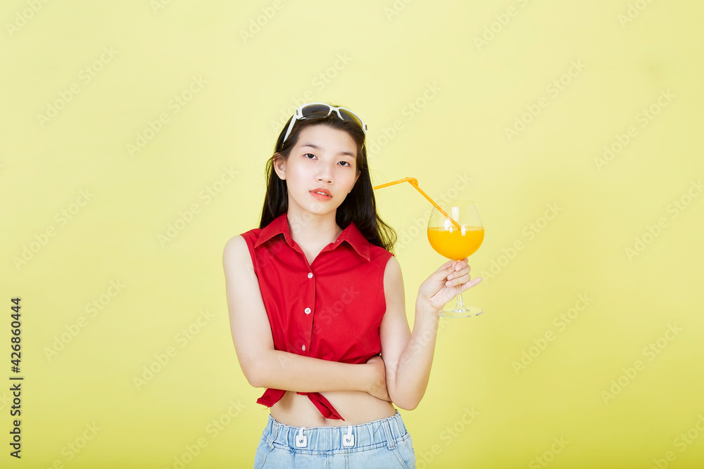 Beautiful cute happy Asian hair brunette woman in summer casual clothes with a glass of fresh fruit juice drink studio shot isolated on colorful a yellow background Beautiful cute happy Asian hair brunette woman in summer casual clothes with a glass of fresh fruit juice drink studio shot isolated on colorful a yellow background