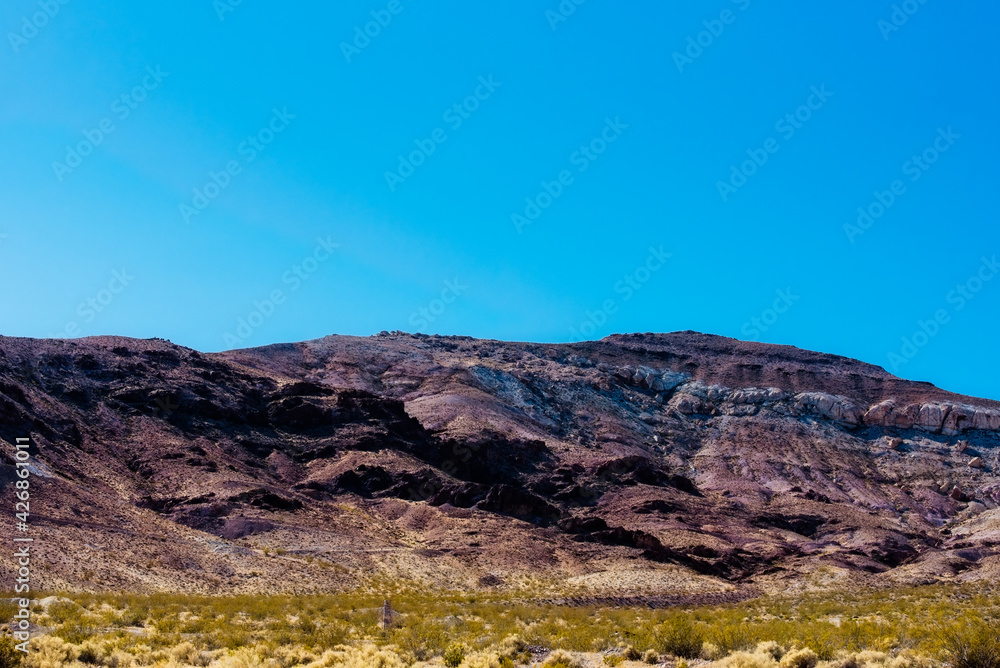 Desert valley floor gives way to relish orange barren Rocky Mountain under a blue sky. Desert valley floor gives way to relish orange barren Rocky Mountain under a blue sky.