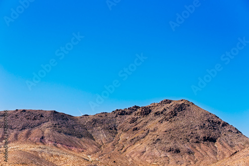 Reddish brown barren mountain peak under bright blue sky.