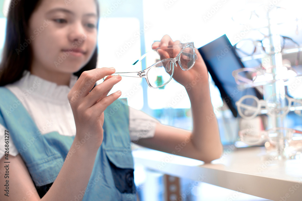Mixed-race child girl choosing glasses in optical shop, selective focus Mixed-race child girl choosing glasses in optical shop, selective focus