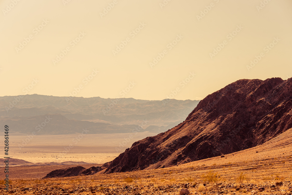 Hot dry desert with barren mountains under a yellow hazy sky.