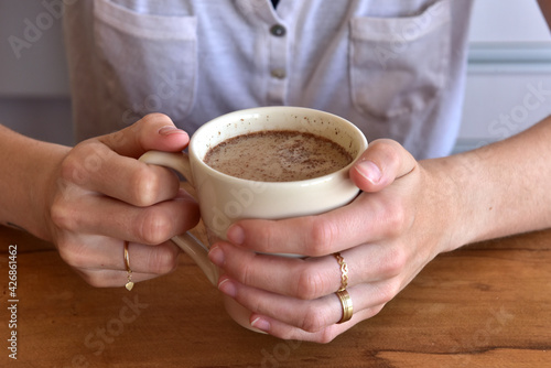 Woman holding cup of coffee with milk and cinnamon powder.