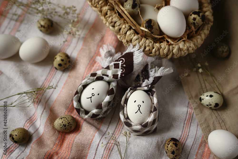 Obraz premium Two Easter eggs in the form of bunnies with a basket of eggs on a napkin. Easter concept.