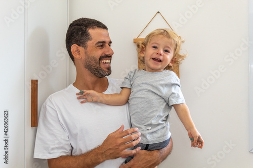 PAI COM FILHO NO COLO E SORRINDO.