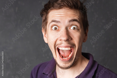 Excited white skinned man smiles opens mouth widely being glad and shocked, rejoices positive news about something. Surprised man in casual clothes can`t believe his great success, good luck or skill