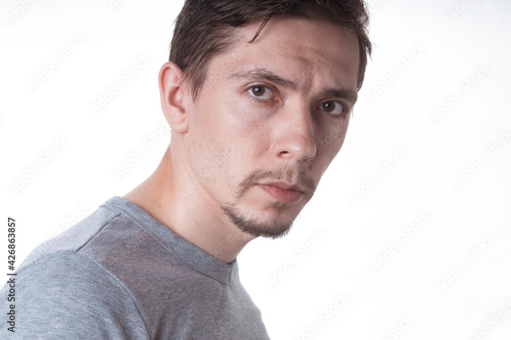 Fototapeta premium Portrait of a sensual young model in unlabeled gray t-shirt posing on white background. Serious man with small beard close-up portrait