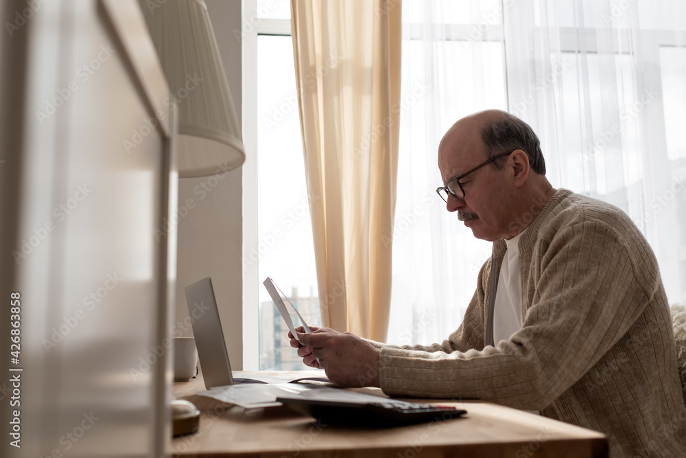 Senior man sitting with paperwork and using calculator while counting money Senior man sitting with paperwork and using calculator while counting money
